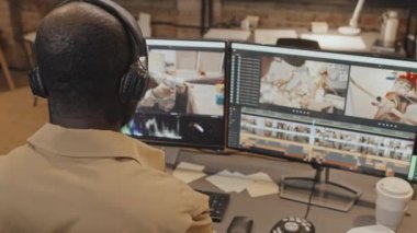 Orta boy Afrika kökenli Amerikalı erkek editörün bilgisayar başında oturması, kulaklıkları ayarlaması ve akşamları ofiste ekrana bakması.