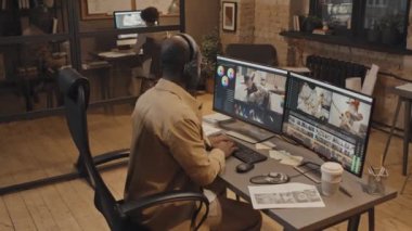 Afrika kökenli Amerikalı erkek ofis çalışanının klavyeye yazı yazıp görüntüyü düzenlemek için renk kontrol panelini kullanmasının yüksek açılı görüntüsü.