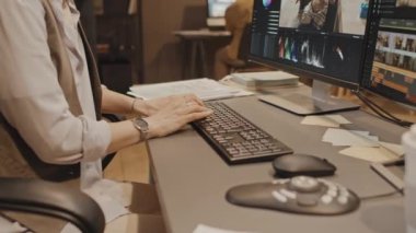 Ofiste masa başında oturan, klavyeye bir şey yazan ve renk derecelendirme kontrolü kullanan beyaz kadının ellerine odaklanın.