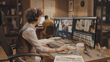 Orta boy beyaz kadın ofis çalışanı iki bilgisayar ekranının montaj görüntülerine bakıyor.