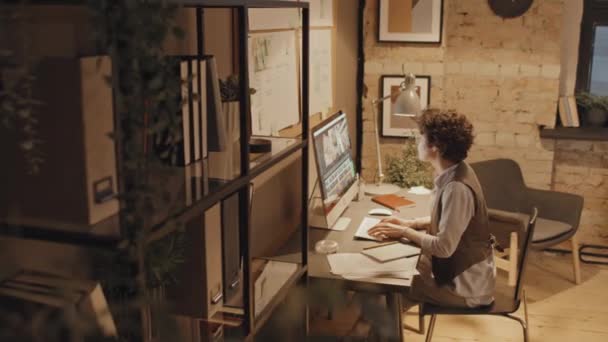 夜間にコンピュータで映像を撮影するデスクに座っている女性の白人オフィスワーカーの高角度フルショット — ストック動画