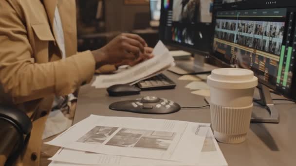 机の上に座っている男性アフリカ系アメリカ人の編集者のティルト ショットは 夜にオフィスでタスクを勉強するプロジェクト文書を調べた — ストック動画