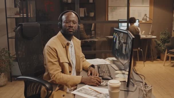 非洲裔美国男性工作人员坐在办公桌前 桌上有文件 计算机和彩色控制工具的中等肖像 — 图库视频影像