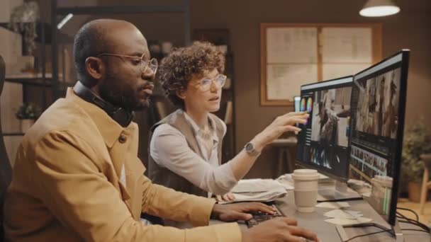 非洲裔美国人和白人男性同事坐在办公桌前讨论视频编辑过程的中景照片 — 图库视频影像