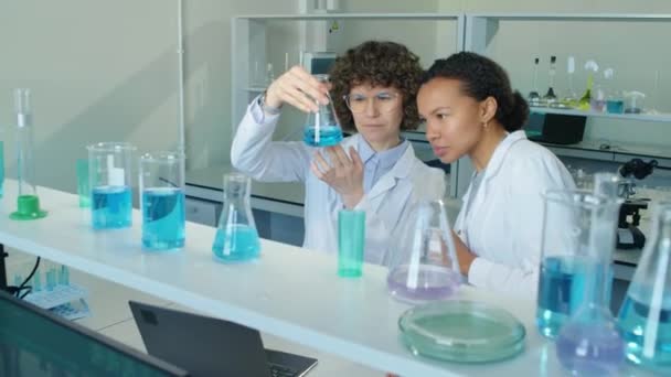 两名白种人和白种人女科学家在白天用蓝色液体看瓶子并在实验室里讨论的中景照片 — 图库视频影像