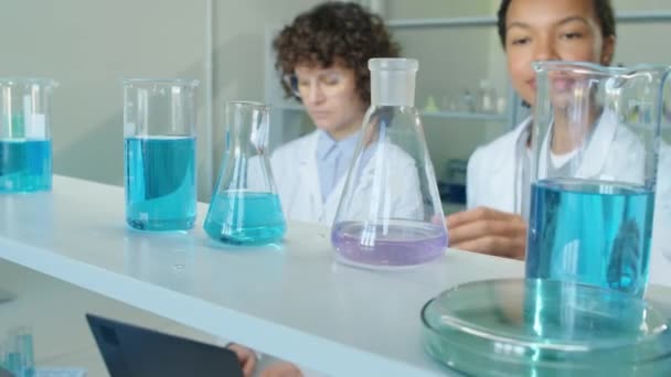 낮에는 실험실 선반에서 보라색 액체와 플라스크를 Biracial 과학자의 — 비디오