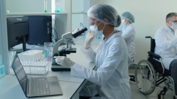 Arc Strzał Biracial Kobieta Naukowiec Siedzi Przy Biurku Patrząc Mikroskopie — Wideo stockowe
