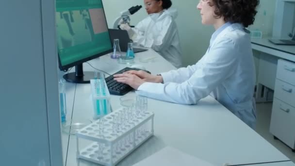 两名从事计算机和显微镜工作的女科学家白天把注意力放在放在放在放在放在实验室桌上的绝密文件夹上 — 图库视频影像
