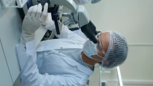 Tıbbi Önlüklü Gözlüklü Saç Filesiyle Laboratuvarda Oturmuş Mikroskoba Bakan Çift — Stok video