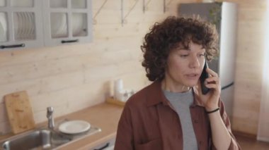 Ani su kesintisi hakkında soru sormak için telefon görüşmesi yapan kızgın Kafkasyalı kadının yüksek açılı orta ölçekli görüntüleri.