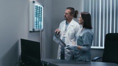 Yetişkin erkek cerrah ve kadın radyolojistin hastaların beyin röntgeni sonuçlarını tartıştığı orta boy bir fotoğraf.