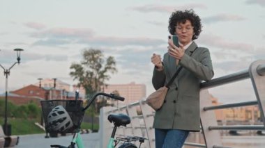 Modern kadın ofis çalışanının sabahın erken saatlerinde dışarıda dikilip görüntülü konuşma görüntüsü.