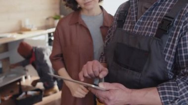 Dijital tablet tutan modern tamircinin seçici odak noktası ve mutfakta durmuş iş tartışan kadın müşteri