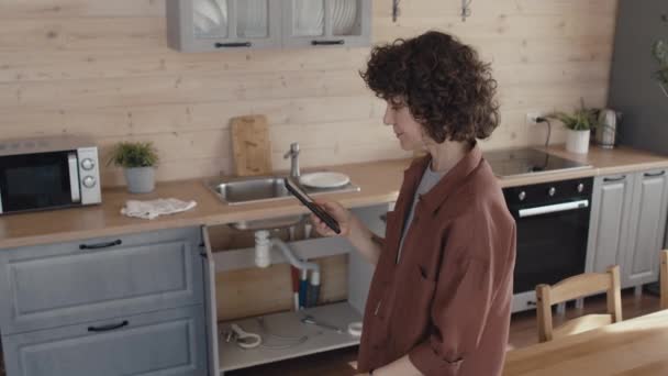 Ώριμη Λευκή Γυναίκα Στέκεται Στην Κουζίνα Ψάχνοντας Για Υδραυλική Επισκευή — Αρχείο Βίντεο