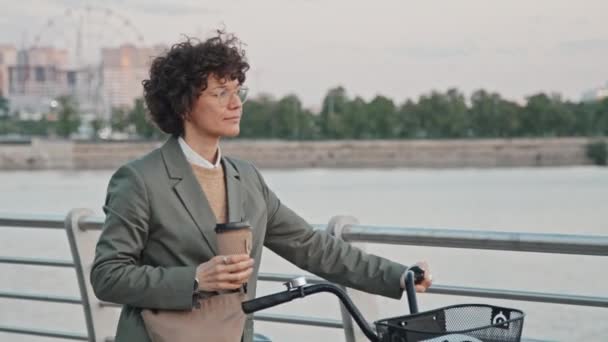 朝早くに川岸沿いの自転車でコーヒーを楽しむ現代のビジネスマンの中長さの追跡ショット — ストック動画