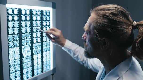 ライトボックスに置かれた深刻な成熟した男性外科医の読書脳X線画像のメディアクローズアップ — ストック動画
