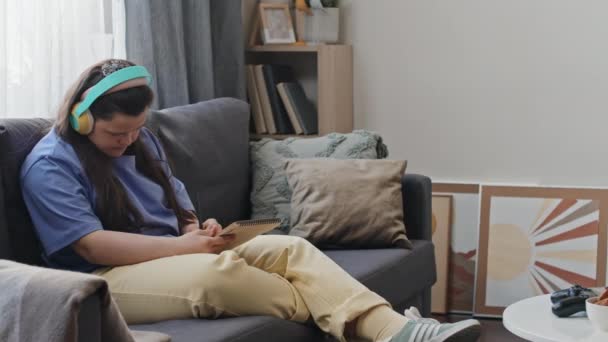 Νεαρή Λευκή Κοπέλα Σύνδρομο Που Φοράει Ακουστικά Κάθεται Στον Καναπέ — Αρχείο Βίντεο