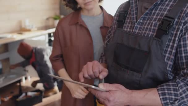 キッチンにデジタルタブレットと女性クライアントを保持する現代修理士の選択的な焦点 作業を議論 — ストック動画