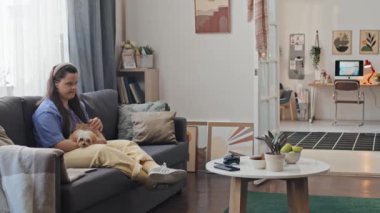 Down sendromlu modern bir kadın oturma odasında oturmuş köpeğini okşuyor ve telefonda biriyle konuşuyor.