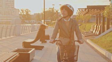 Gündoğumunda bisiklet kaskı takıp işe bisikletle giden modern iş kadınının resmi.