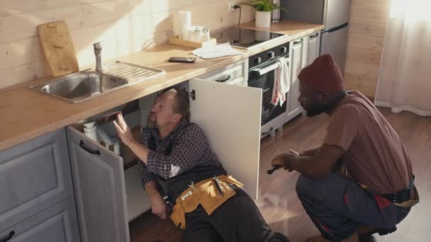 High Angle Two Ethnically Diverse Plumbers Working Clients Kitchen Discussing — Stock Video