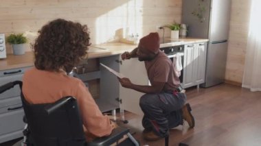 Afro-Amerikalı tesisatçı elinde kağıt ile engelli kadın müşterilerle hizmet listesini tartışıyor.