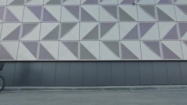 Düşük açılı, modern, beyaz kadın bisikletiyle caddede yürürken modern dış görünüşlü bir binanın önünden geçerken.