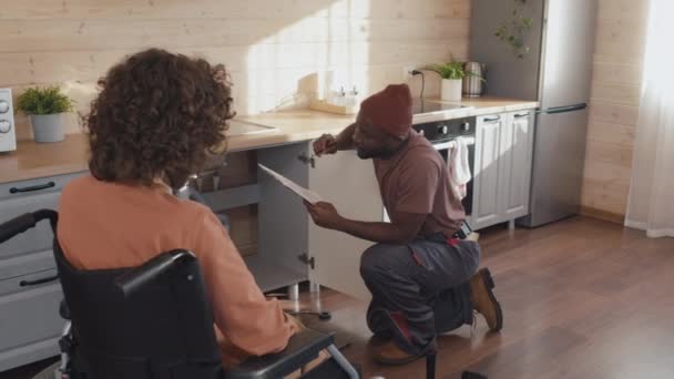 Afroamerykańska Hydraulik Trzymając Schowek Dokumentami Omawiającymi Listę Usług Klientką Niepełnosprawną — Wideo stockowe