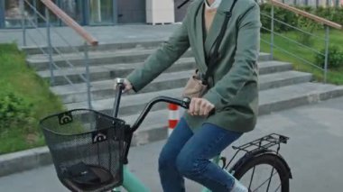 Beyaz kadın, kıvırcık saçlı, kask takıyor ve bisiklet sürüyor.