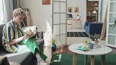 Engelli bir kadının oturma odasındaki kanepede oturmuş resim çizerken görüntüsü.