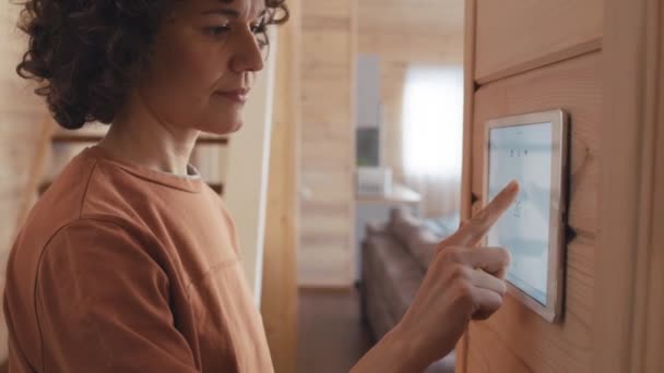 壁にタブレットを使用して屋内温度を変更するホームオートメーションシステムを装備した現代木造の家に住む白人女性の選択的な焦点ショット — ストック動画