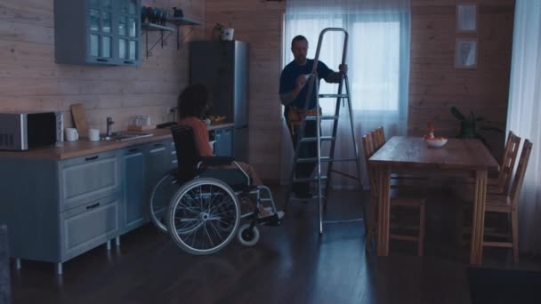 两名不同族裔的杂工在残疾妇女的家里干活 其中一人在厨房里更换灯泡 — 图库视频影像