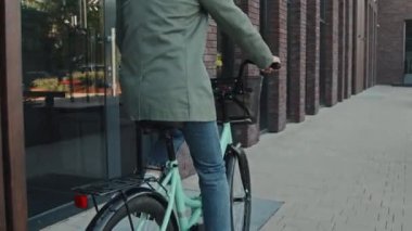 Modern şehrin caddesinde bisiklet süren, kıvırcık saçlı, şık günlük kıyafetler giyen tanınmamış iş kadınının fotoğrafını çek.