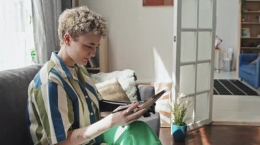 Oturma odasında oturmuş çizim defterine resim çizen protez kollu genç bir kadının orta ölçekli görüntüsü.