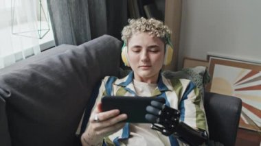 Yüksek açılı orta açılı, engelli kız kol protezi takıyor ve akıllı telefondan internet 'te müzik videosu izlerken eğleniyor.