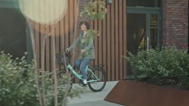 Neşeli beyaz kadın ofis çalışanının sokak boyunca bisiklet sürerken giydiği günlük kıyafetlerin izini sürüyorum.