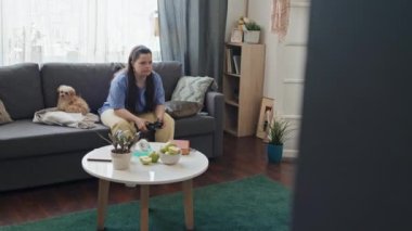 Down sendromlu genç bir kadının oturma odasında kanepede oturup video oyunu oynaması.