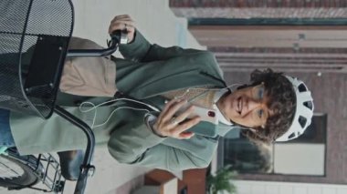 Dışarıda kulaklık takan neşeli bayan yöneticinin dikey orta boy portresi video konuşmasında bisikletiyle konuşuyor.