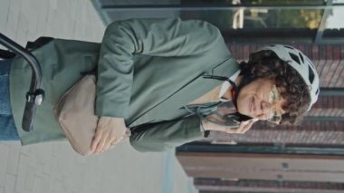 Dikey orta boy, neşeli, kıvırcık saçlı, bisiklet kaskı takan, dışarıda telefonla konuşan beyaz bir kadın.