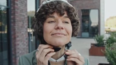 Beyaz kadın ofis çalışanı dışarıda duruyor kaskını takıyor ve bisiklete biniyor.