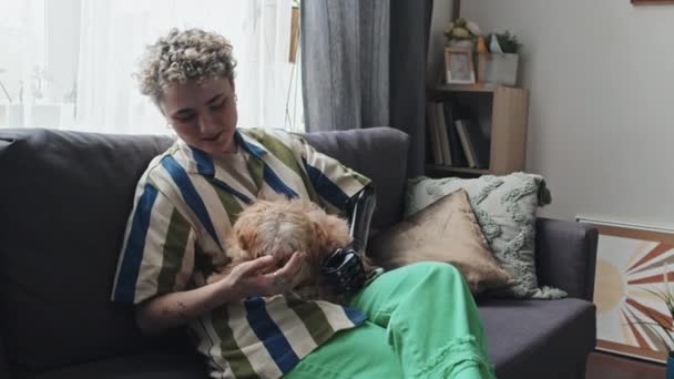 快乐的残疾年轻女子坐在客厅的沙发上 爱抚她可爱的狗 — 图库视频影像