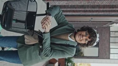 Dikey orta boy beyaz kadın portresi şık şık günlük kıyafetler giymiş gözlüklü ve kasklı dışarıda bisikletle kameraya poz veriyor.