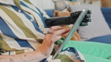 Özürlü, tanınmayan, protez kol takan dijital tablette internette sörf yapan genç bir kadının seçici odağı.