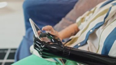 Oturma odasında oturmuş dijital tablet üzerinde internette sörf yapan protez kollu tanınmayan bir kadının seçmeli odak fotoğrafı.