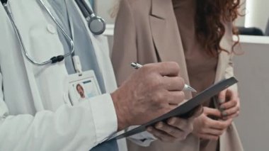 Yetişkin beyaz pratisyen ve genç hastasının hastane lobisinde durup test sonuçlarını tartışırkenki görüntüsü.