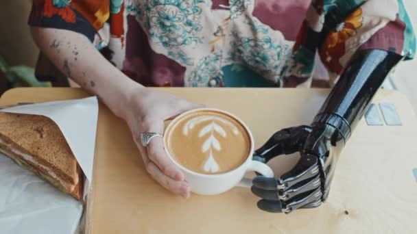 现代咖啡店中戴假臂 身披假肢 身无分文的年轻残疾妇女坐在餐桌旁 喝着卡布奇诺咖啡的高角度中特写 — 图库视频影像