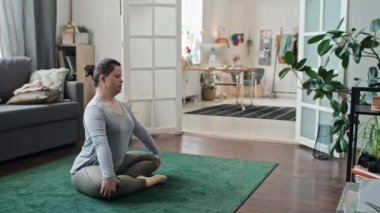 Down sendromlu modern bir kadın oturma odasında oturmuş yoga yapıyor.