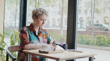 Özürlü, şık kıyafetler giyen, cafe masasında oturmuş akıllı telefondan öğle yemeğinin fotoğrafını çeken modern nesil Z kızı.