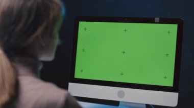 Gece vakti yeşil ekranı açık bir şekilde bilgisayar ekranının önünde oturan tanınmayan kadını kapatın.