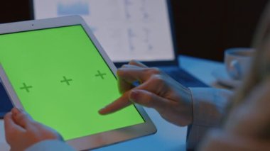 Elinde yeşil ekranla tableti tutan ve işaret parmağını aşağı yukarı hareket ettiren tanımlanamayan kadını kapatın.